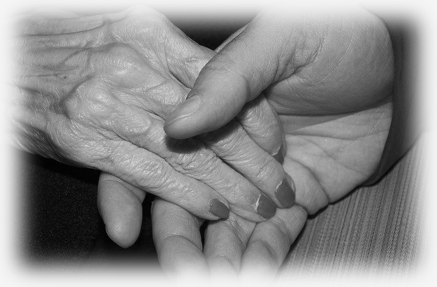 A man's hand gently holds the hand of an elderly woman